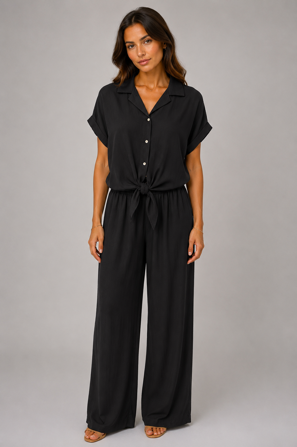 Woman modelling a Made in Italy two-piece lounge set in a soft textured fabric. The outfit features a relaxed short-sleeve collared shirt with button-front detail and a tie-front hem, paired with wide-leg elasticated waist trousers. Shown in multiple colours against a light grey studio background.