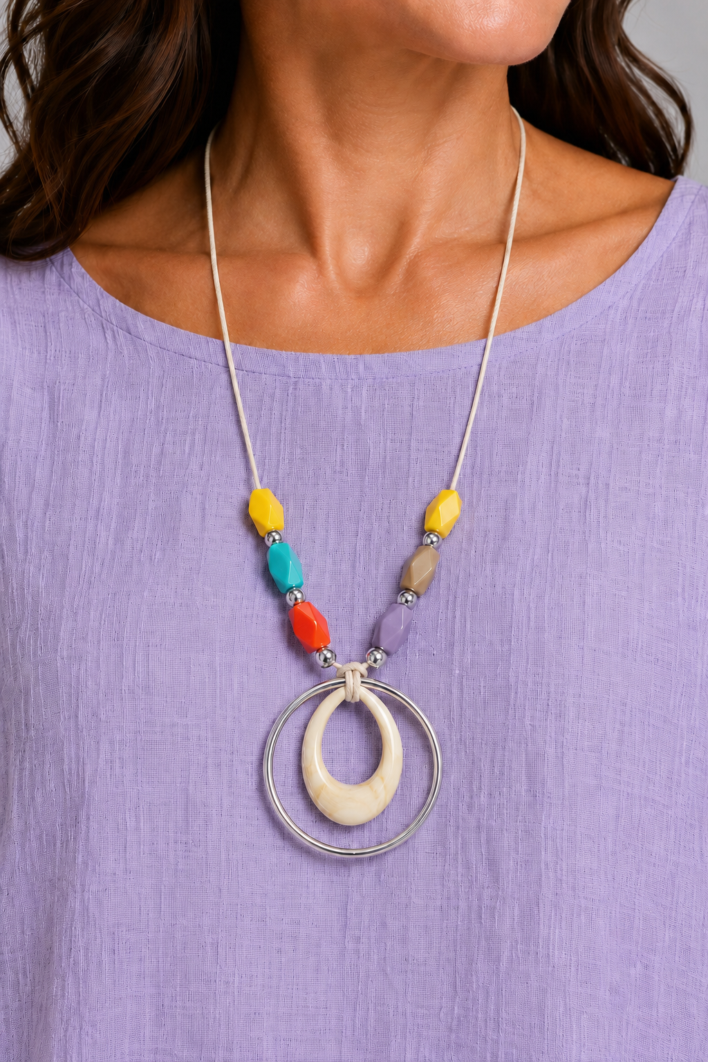 Close-up of long cord necklace with multicoloured beads, cream wood-effect teardrop pendant and large silver hoop.