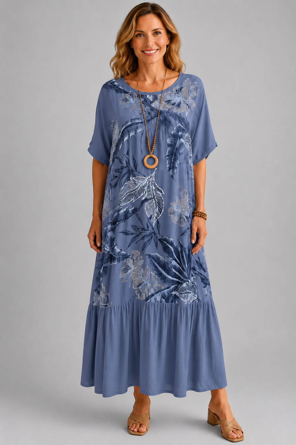 Woman modelling a navy blue Italian maxi dress with tonal tropical leaf print, round neckline, short sleeves, tiered hem and relaxed oversized fit on a light grey studio background.