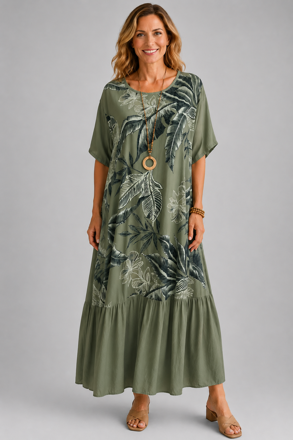 Woman modelling a navy blue Italian maxi dress with tonal tropical leaf print, round neckline, short sleeves, tiered hem and relaxed oversized fit on a light grey studio background.