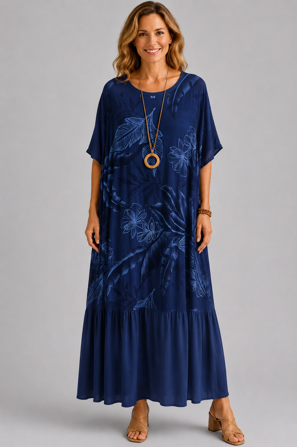 Woman modelling a navy blue Italian maxi dress with tonal tropical leaf print, round neckline, short sleeves, tiered hem and relaxed oversized fit on a light grey studio background.