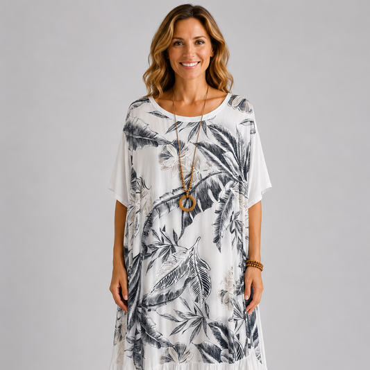 Woman modelling a navy blue Italian maxi dress with tonal tropical leaf print, round neckline, short sleeves, tiered hem and relaxed oversized fit on a light grey studio background.