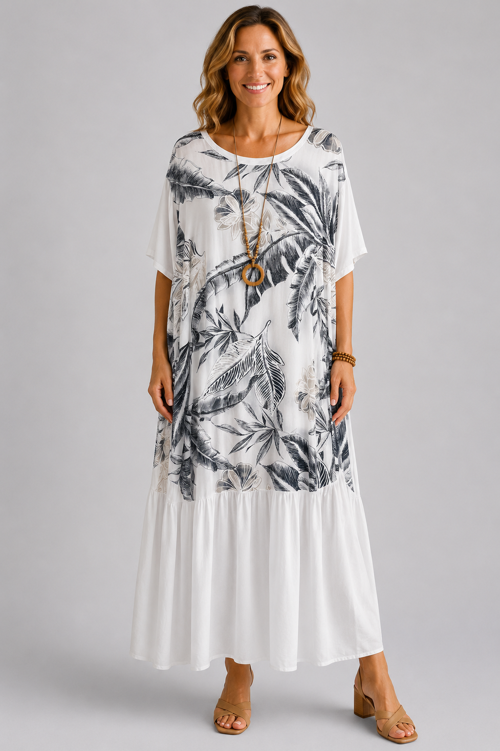 Woman modelling a navy blue Italian maxi dress with tonal tropical leaf print, round neckline, short sleeves, tiered hem and relaxed oversized fit on a light grey studio background.