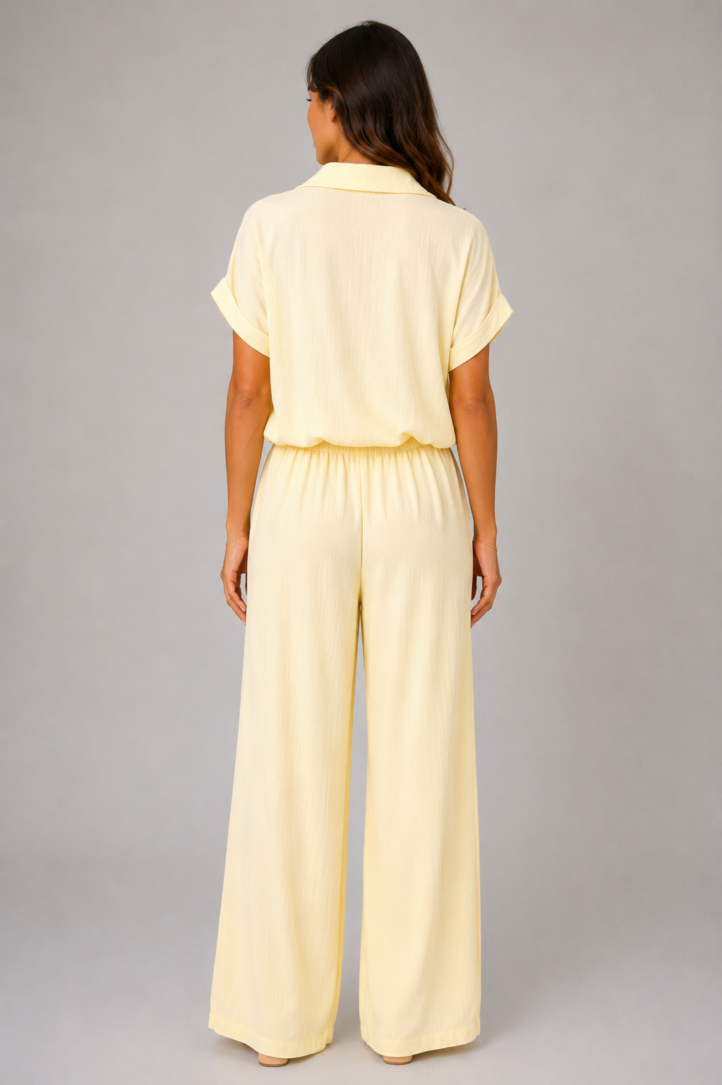 Woman modelling a Made in Italy two-piece lounge set in a soft textured fabric. The outfit features a relaxed short-sleeve collared shirt with button-front detail and a tie-front hem, paired with wide-leg elasticated waist trousers. Shown in multiple colours against a light grey studio background.