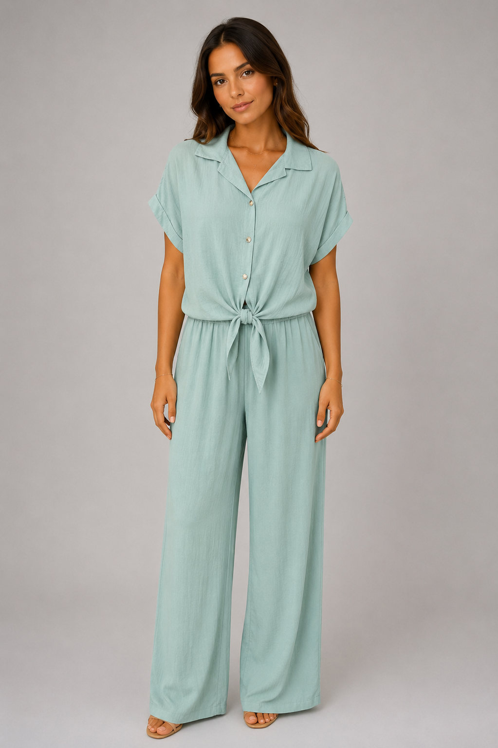 Woman modelling a Made in Italy two-piece lounge set in a soft textured fabric. The outfit features a relaxed short-sleeve collared shirt with button-front detail and a tie-front hem, paired with wide-leg elasticated waist trousers. Shown in multiple colours against a light grey studio background.
