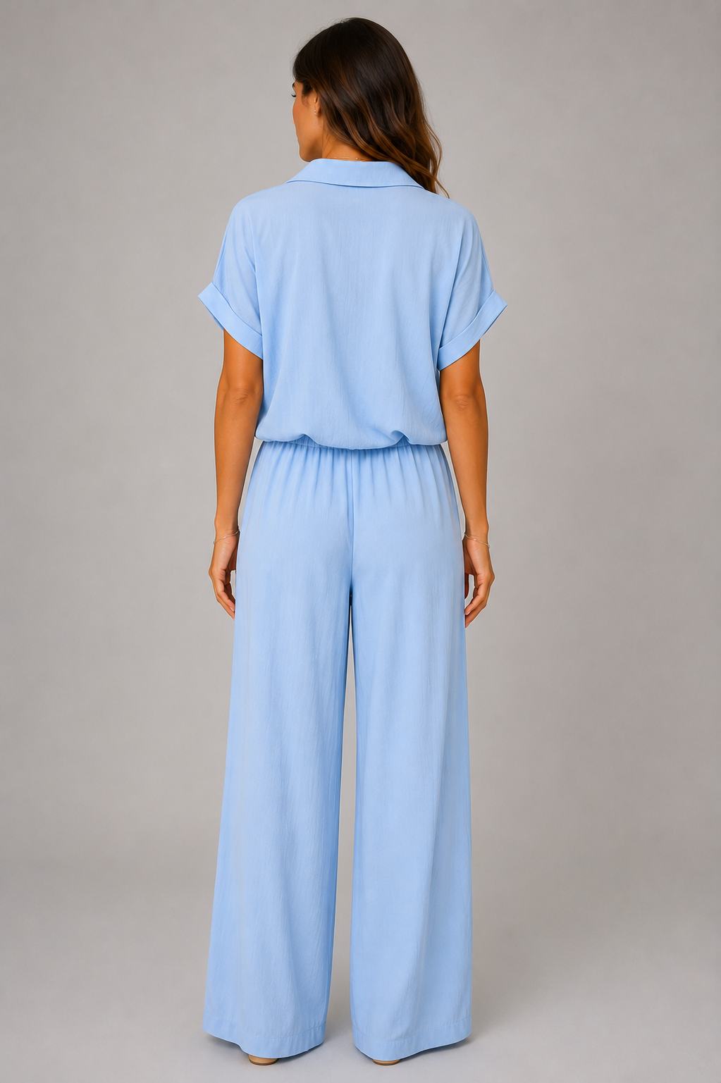 Woman modelling a Made in Italy two-piece lounge set in a soft textured fabric. The outfit features a relaxed short-sleeve collared shirt with button-front detail and a tie-front hem, paired with wide-leg elasticated waist trousers. Shown in multiple colours against a light grey studio background.