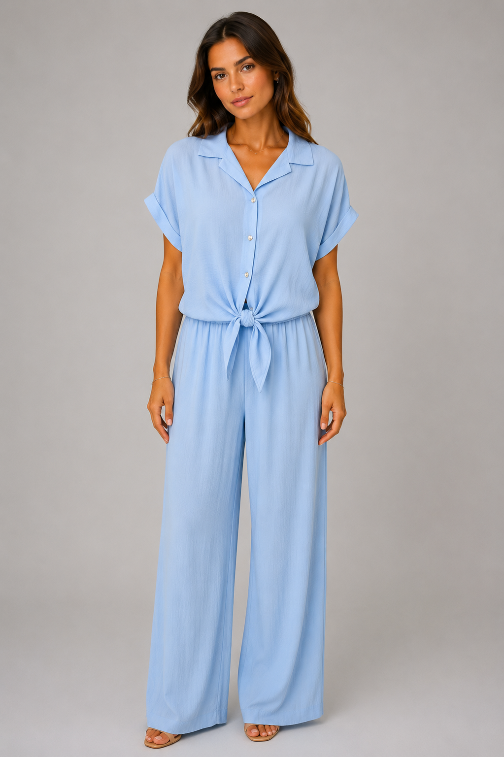 Woman modelling a Made in Italy two-piece lounge set in a soft textured fabric. The outfit features a relaxed short-sleeve collared shirt with button-front detail and a tie-front hem, paired with wide-leg elasticated waist trousers. Shown in multiple colours against a light grey studio background.