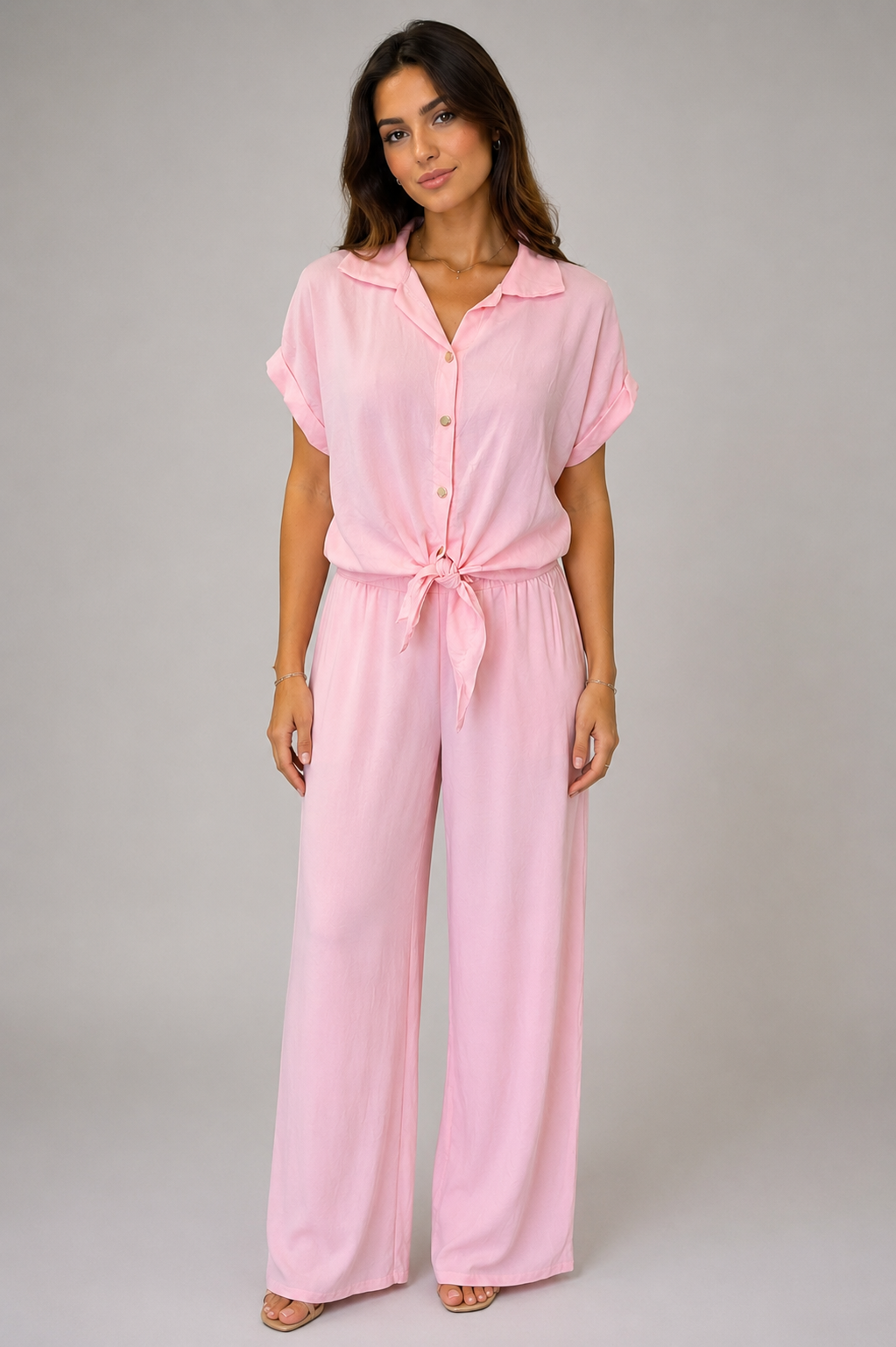 Woman modelling a Made in Italy two-piece lounge set in a soft textured fabric. The outfit features a relaxed short-sleeve collared shirt with button-front detail and a tie-front hem, paired with wide-leg elasticated waist trousers. Shown in multiple colours against a light grey studio background.