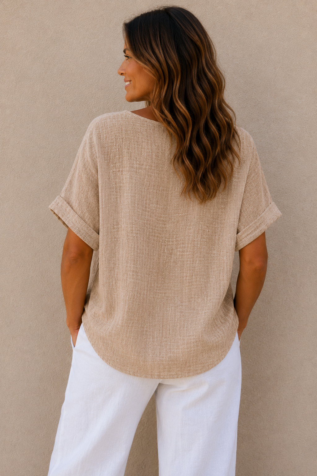 Woman wearing a relaxed-fit textured gauze top with rolled short sleeves and a scoop neckline, paired with white linen pants. Shown from both front and back views against a neutral background, highlighting the lightweight fabric, loose silhouette, and curved hem. One size fit suitable up to a size 16.