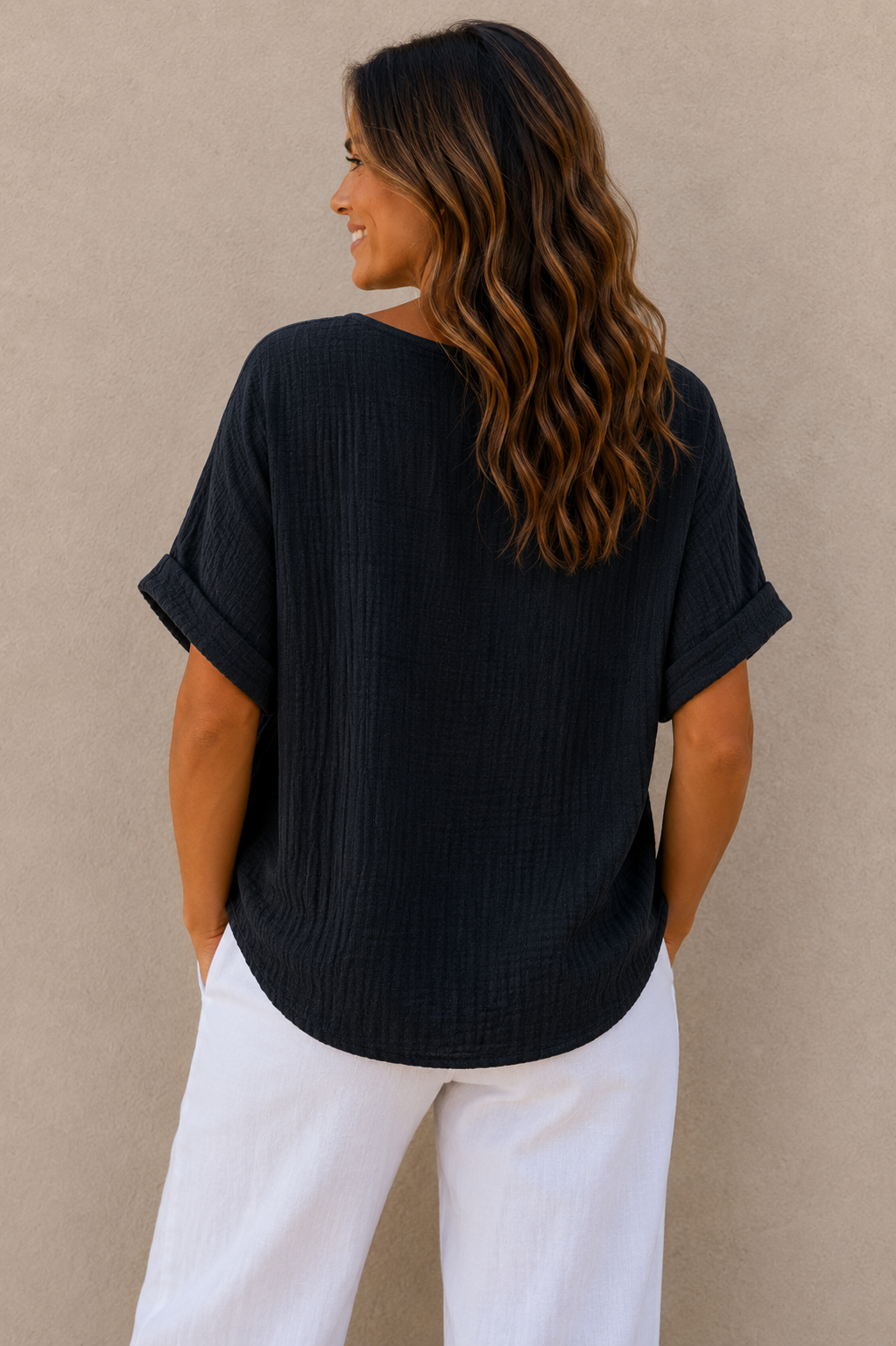 Woman wearing a relaxed-fit textured gauze top with rolled short sleeves and a scoop neckline, paired with white linen pants. Shown from both front and back views against a neutral background, highlighting the lightweight fabric, loose silhouette, and curved hem. One size fit suitable up to a size 16.
