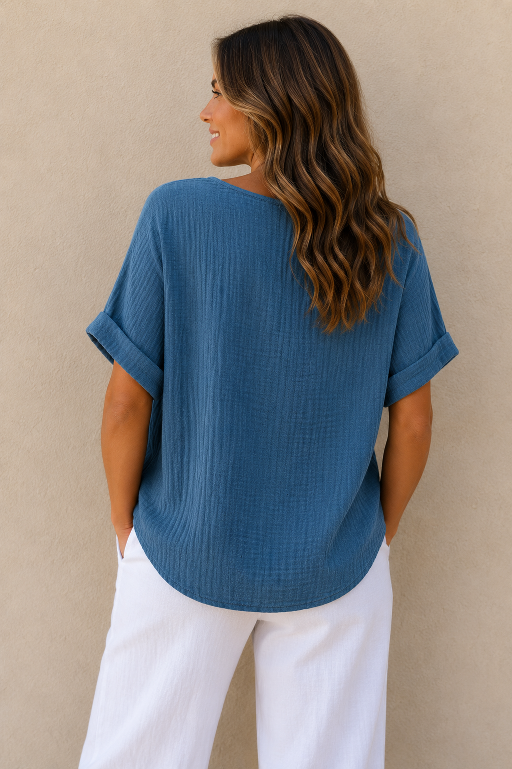 Woman wearing a relaxed-fit textured gauze top with rolled short sleeves and a scoop neckline, paired with white linen pants. Shown from both front and back views against a neutral background, highlighting the lightweight fabric, loose silhouette, and curved hem. One size fit suitable up to a size 16.