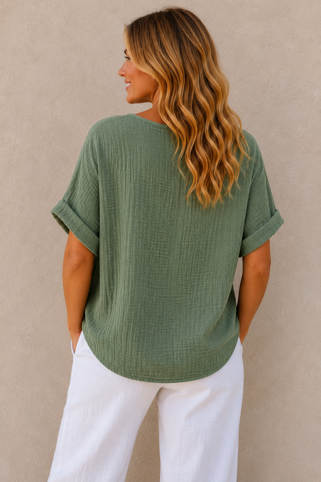 Woman wearing a relaxed-fit textured gauze top with rolled short sleeves and a scoop neckline, paired with white linen pants. Shown from both front and back views against a neutral background, highlighting the lightweight fabric, loose silhouette, and curved hem. One size fit suitable up to a size 16.