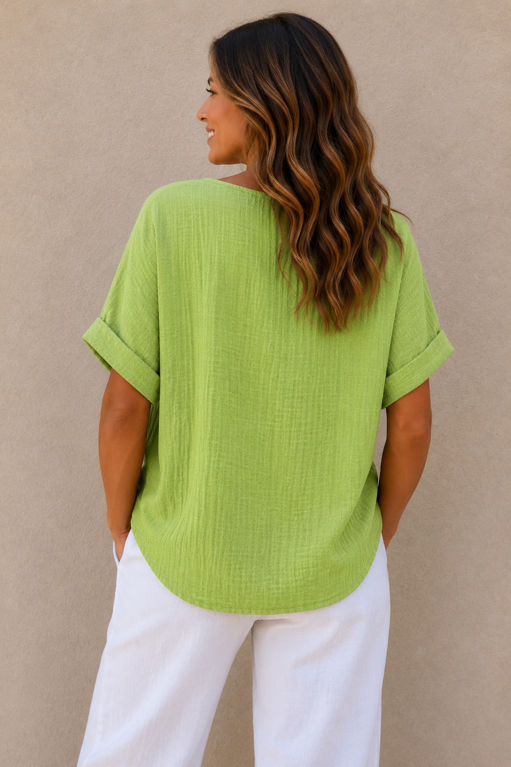 Woman wearing a relaxed-fit textured gauze top with rolled short sleeves and a scoop neckline, paired with white linen pants. Shown from both front and back views against a neutral background, highlighting the lightweight fabric, loose silhouette, and curved hem. One size fit suitable up to a size 16.