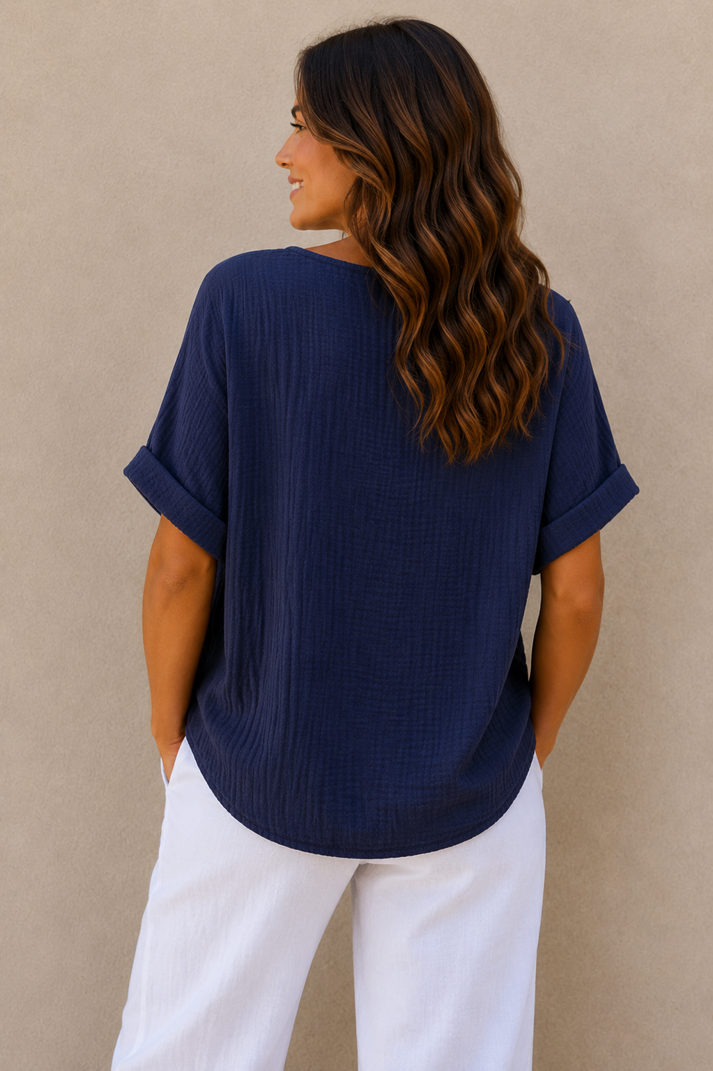 Woman wearing a relaxed-fit textured gauze top with rolled short sleeves and a scoop neckline, paired with white linen pants. Shown from both front and back views against a neutral background, highlighting the lightweight fabric, loose silhouette, and curved hem. One size fit suitable up to a size 16.
