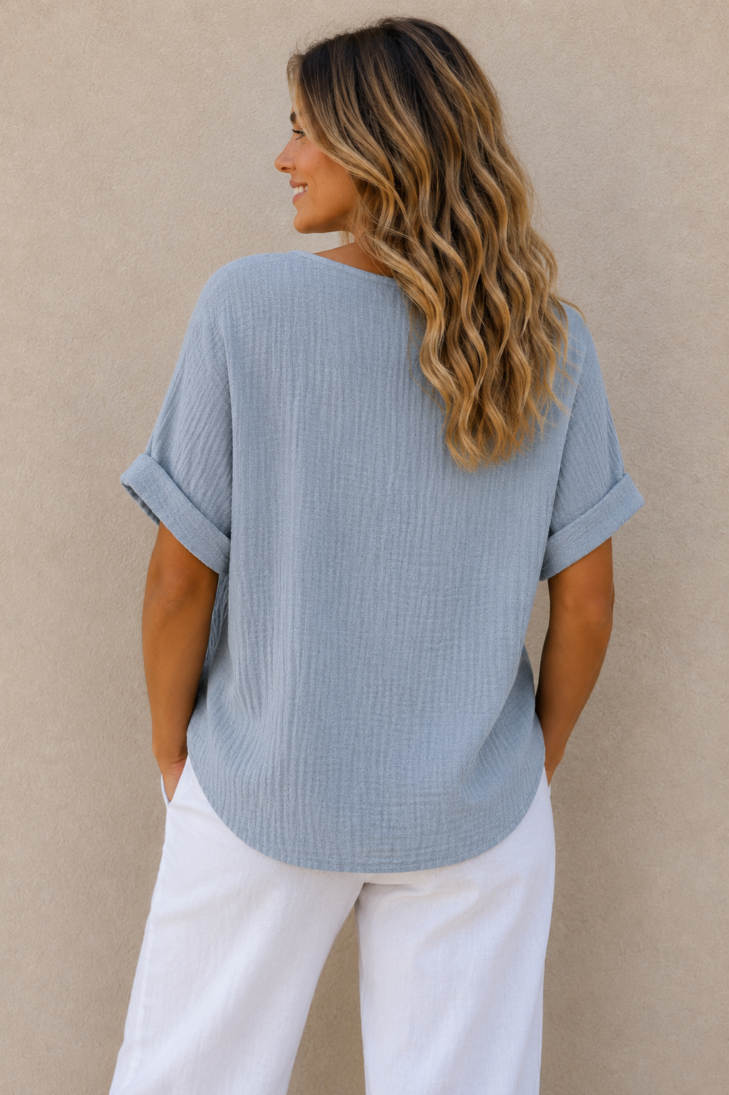Woman wearing a relaxed-fit textured gauze top with rolled short sleeves and a scoop neckline, paired with white linen pants. Shown from both front and back views against a neutral background, highlighting the lightweight fabric, loose silhouette, and curved hem. One size fit suitable up to a size 16.