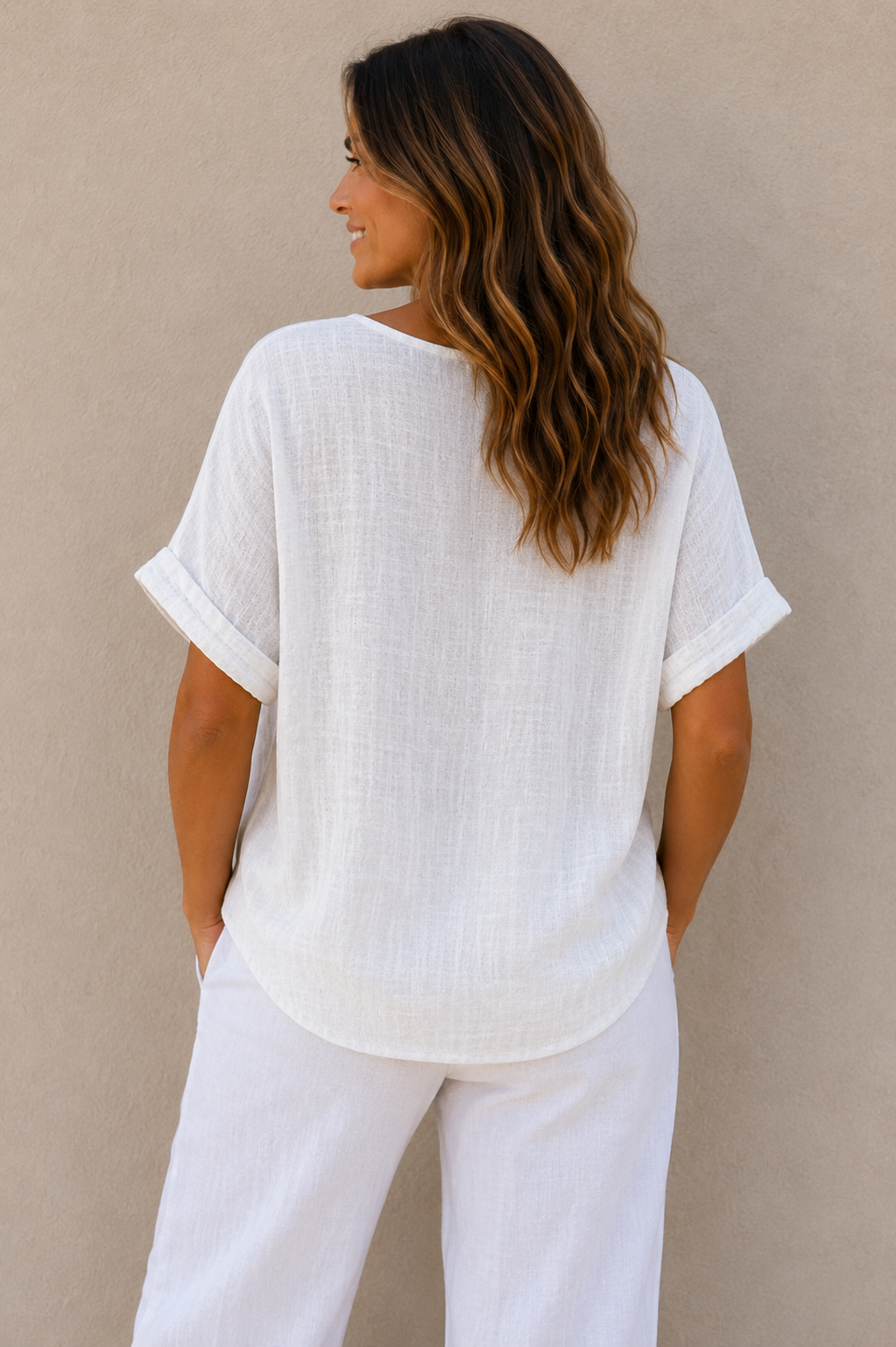 Woman wearing a relaxed-fit textured gauze top with rolled short sleeves and a scoop neckline, paired with white linen pants. Shown from both front and back views against a neutral background, highlighting the lightweight fabric, loose silhouette, and curved hem. One size fit suitable up to a size 16.