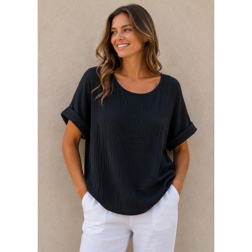 Woman wearing a relaxed-fit textured gauze top with rolled short sleeves and a scoop neckline, paired with white linen pants. Shown from both front and back views against a neutral background, highlighting the lightweight fabric, loose silhouette, and curved hem. One size fit suitable up to a size 16.