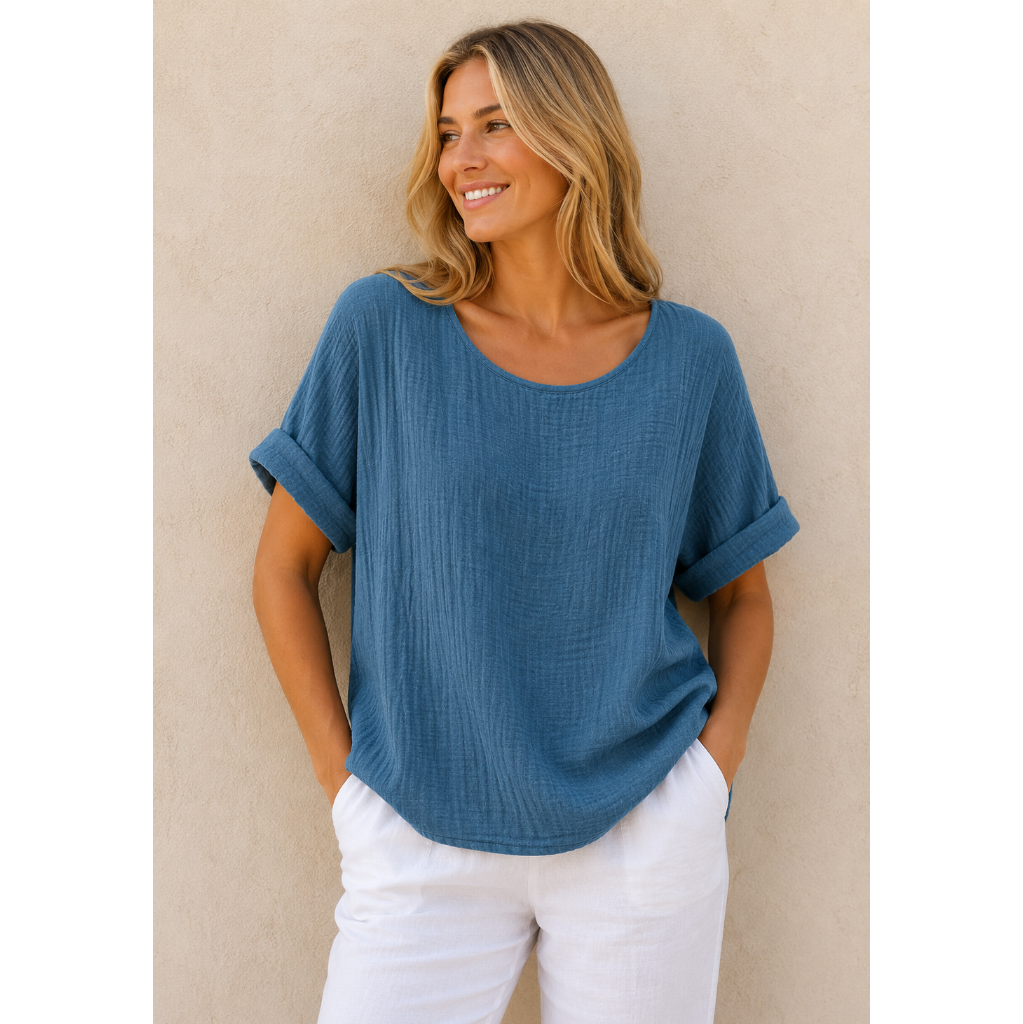 Woman wearing a relaxed-fit textured gauze top with rolled short sleeves and a scoop neckline, paired with white linen pants. Shown from both front and back views against a neutral background, highlighting the lightweight fabric, loose silhouette, and curved hem. One size fit suitable up to a size 16.
