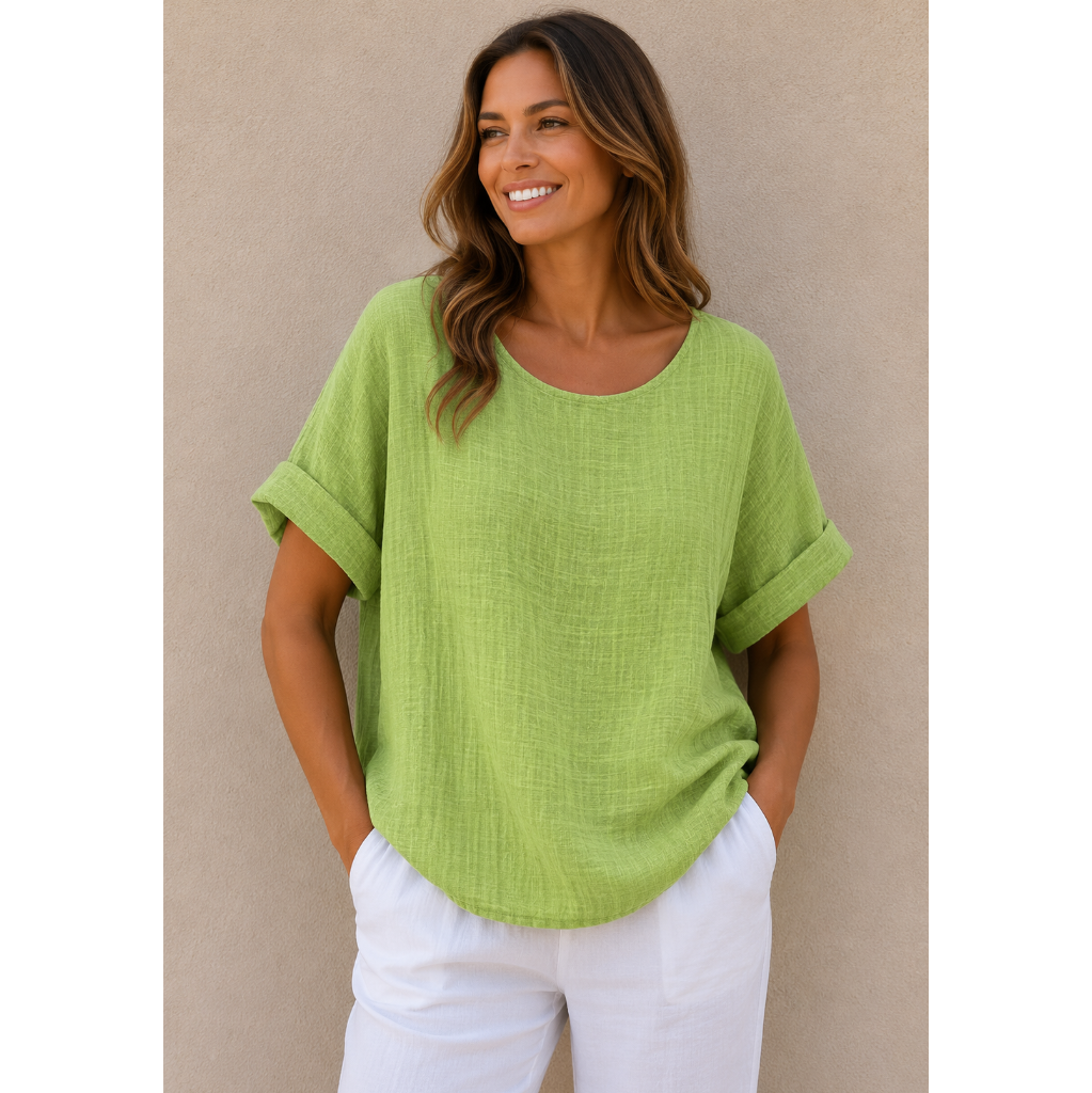 Woman wearing a relaxed-fit textured gauze top with rolled short sleeves and a scoop neckline, paired with white linen pants. Shown from both front and back views against a neutral background, highlighting the lightweight fabric, loose silhouette, and curved hem. One size fit suitable up to a size 16.