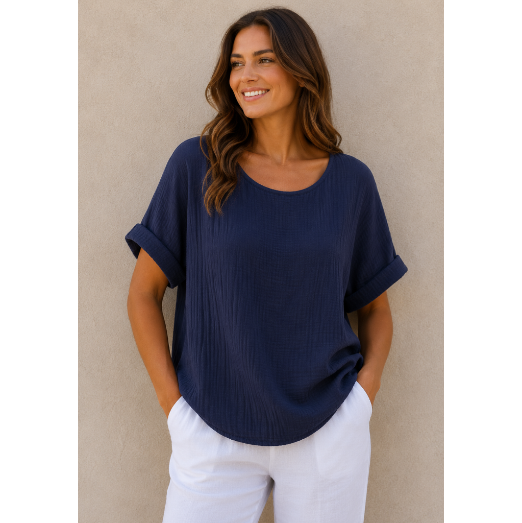 Woman wearing a relaxed-fit textured gauze top with rolled short sleeves and a scoop neckline, paired with white linen pants. Shown from both front and back views against a neutral background, highlighting the lightweight fabric, loose silhouette, and curved hem. One size fit suitable up to a size 16.