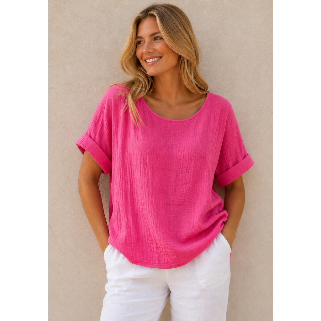Woman wearing a relaxed-fit textured gauze top with rolled short sleeves and a scoop neckline, paired with white linen pants. Shown from both front and back views against a neutral background, highlighting the lightweight fabric, loose silhouette, and curved hem. One size fit suitable up to a size 16.