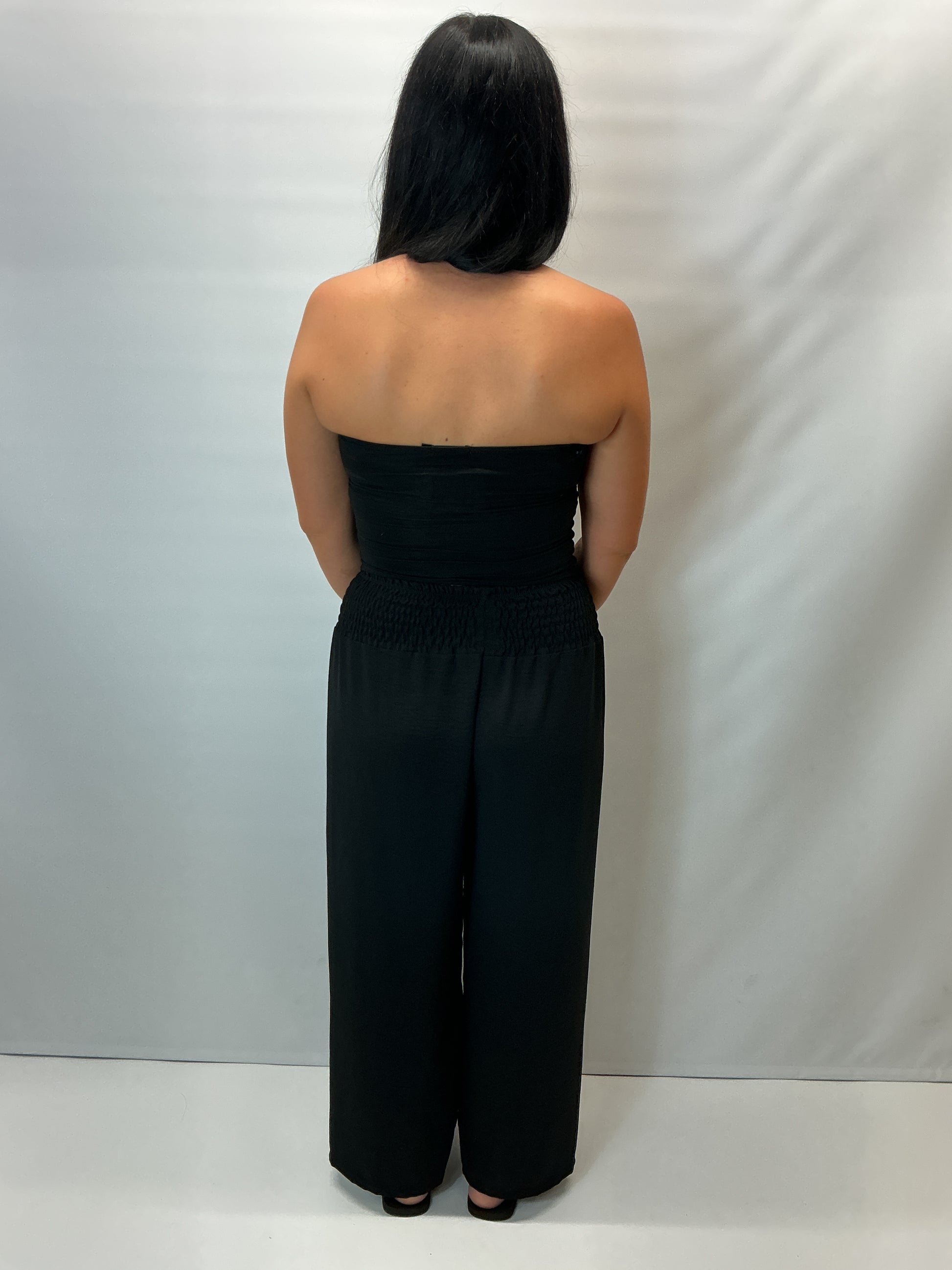 Black smocked waist wide leg trousers with a relaxed fit, shown on a model wearing a fitted black halter top.