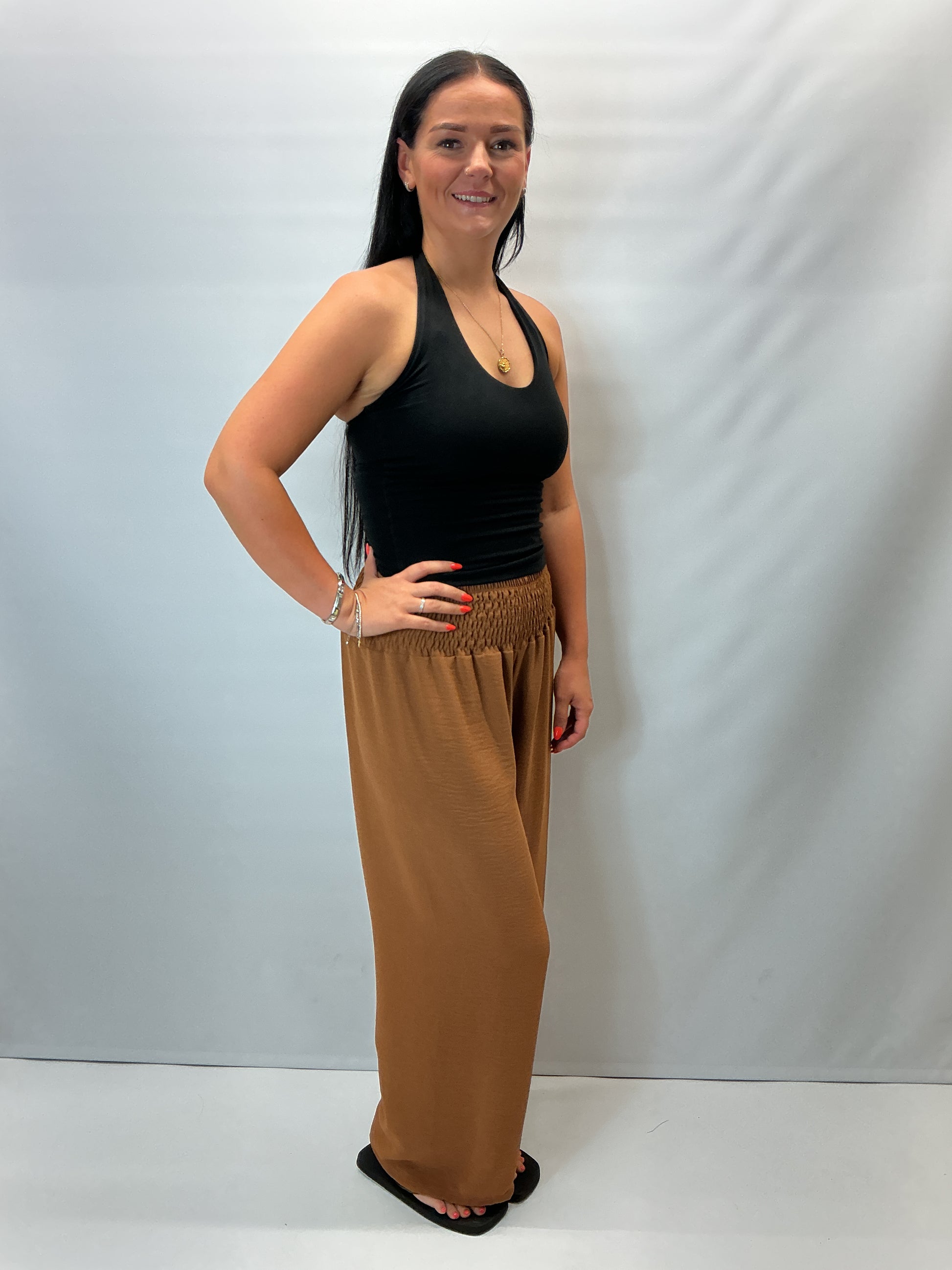 Camel smocked waist wide leg trousers with a relaxed fit, shown on a model wearing a fitted black halter top.