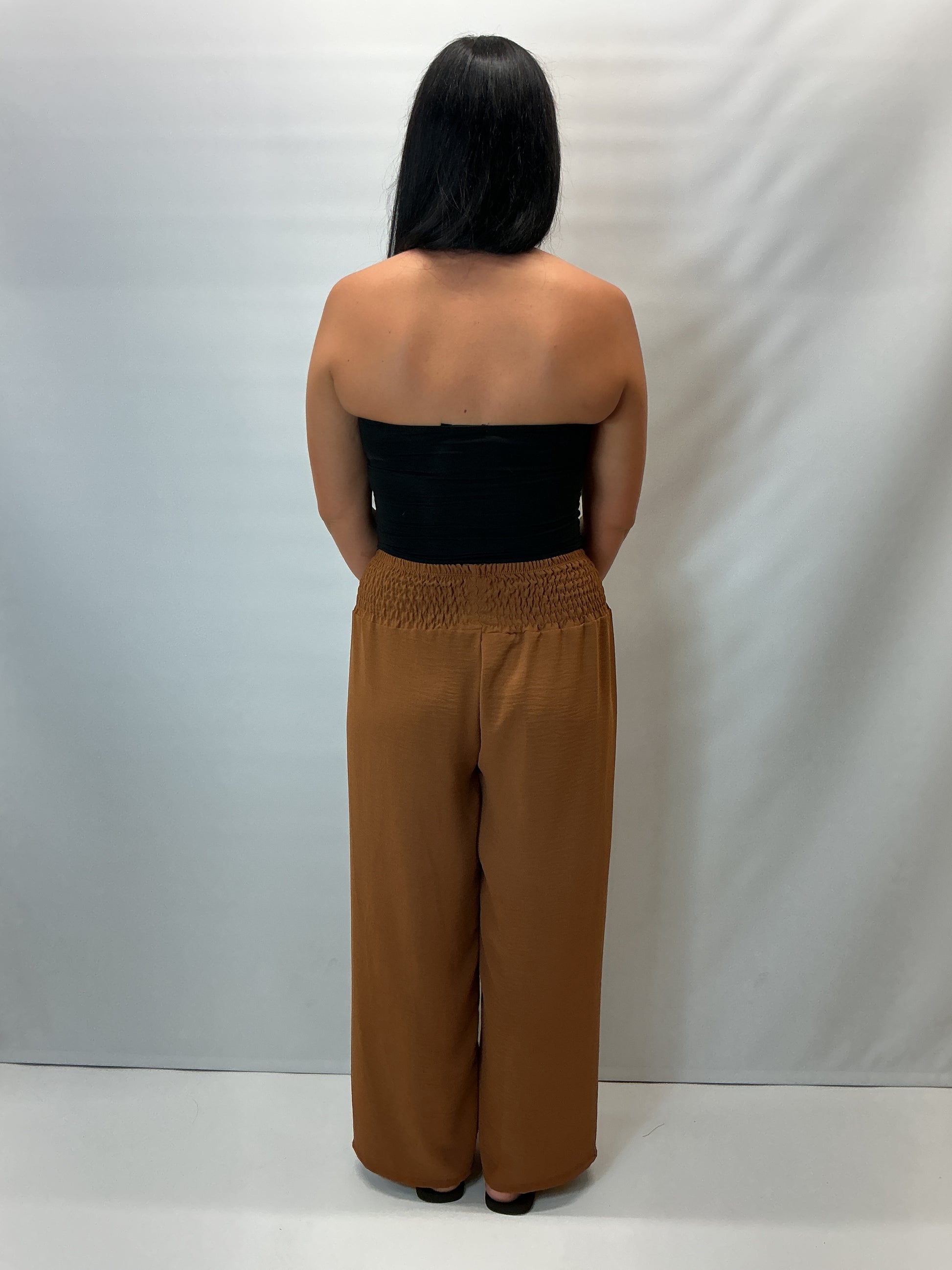 Camel smocked waist wide leg trousers with a relaxed fit, shown on a model wearing a fitted black halter top.
