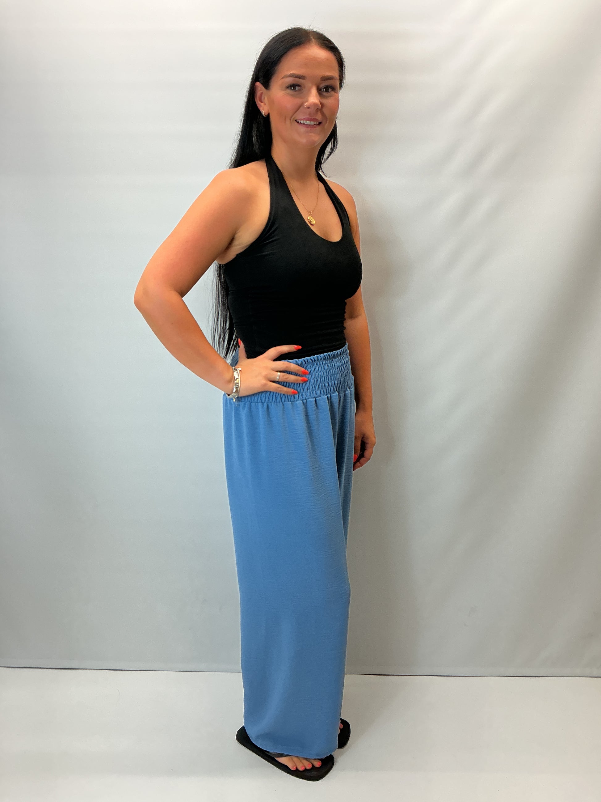 Denim Blue smocked waist wide leg trousers with a relaxed fit, shown on a model wearing a fitted black halter top.