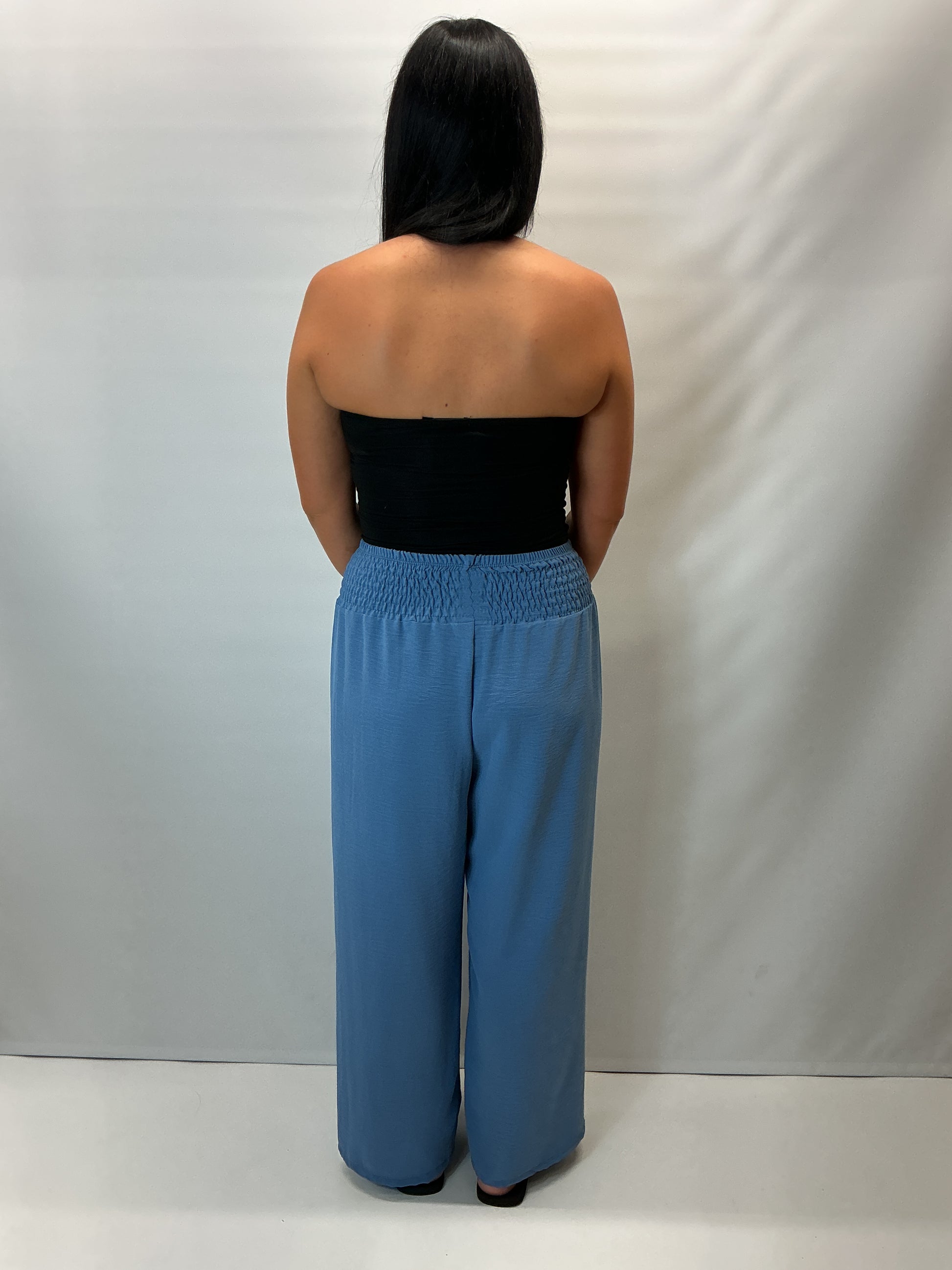 Denim Blue smocked waist wide leg trousers with a relaxed fit, shown on a model wearing a fitted black halter top.