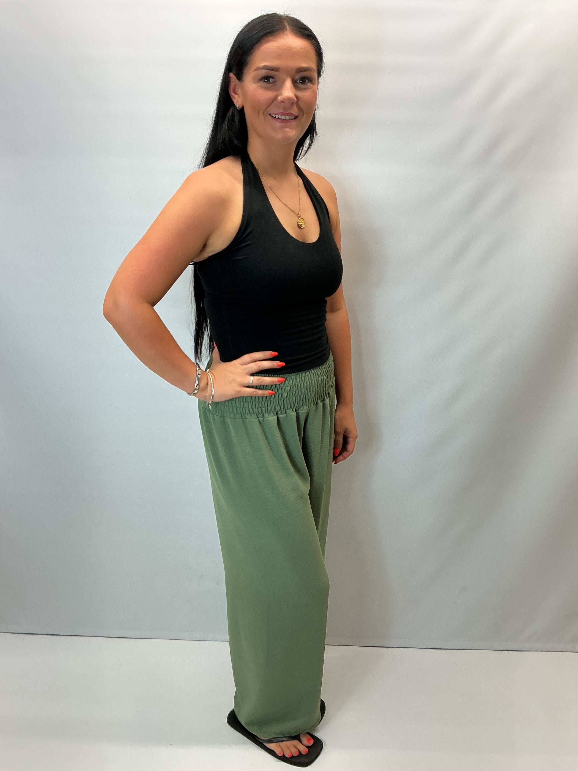 Khaki Green smocked waist wide leg trousers with a relaxed fit, shown on a model wearing a fitted black halter top.