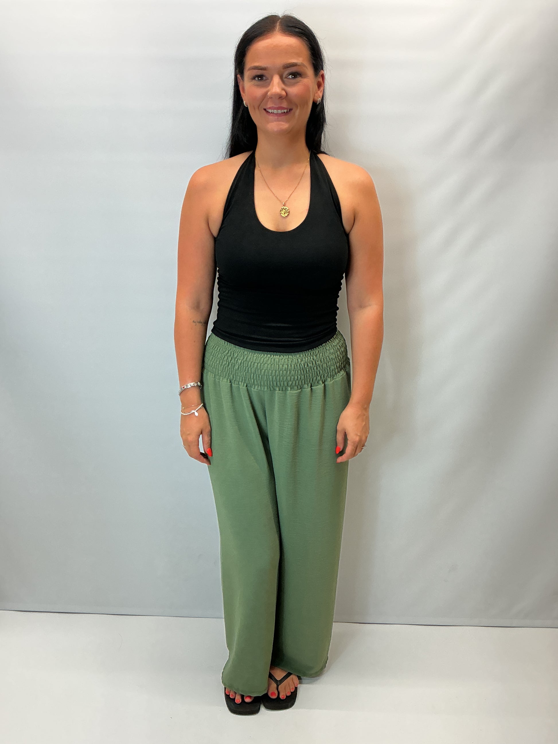 Khaki Green smocked waist wide leg trousers with a relaxed fit, shown on a model wearing a fitted black halter top.