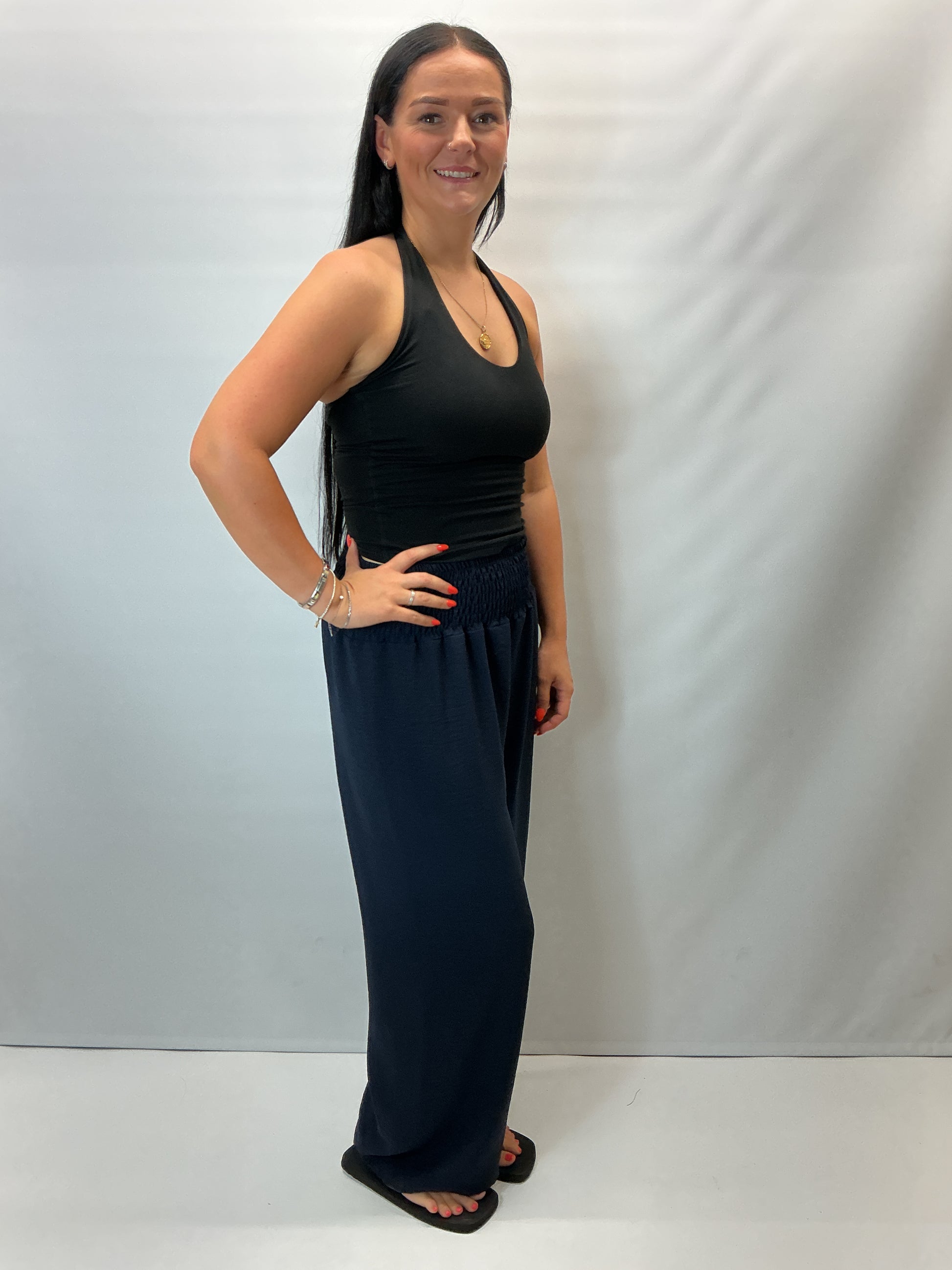 Navy smocked waist wide leg trousers with a relaxed fit, shown on a model wearing a fitted black halter top.