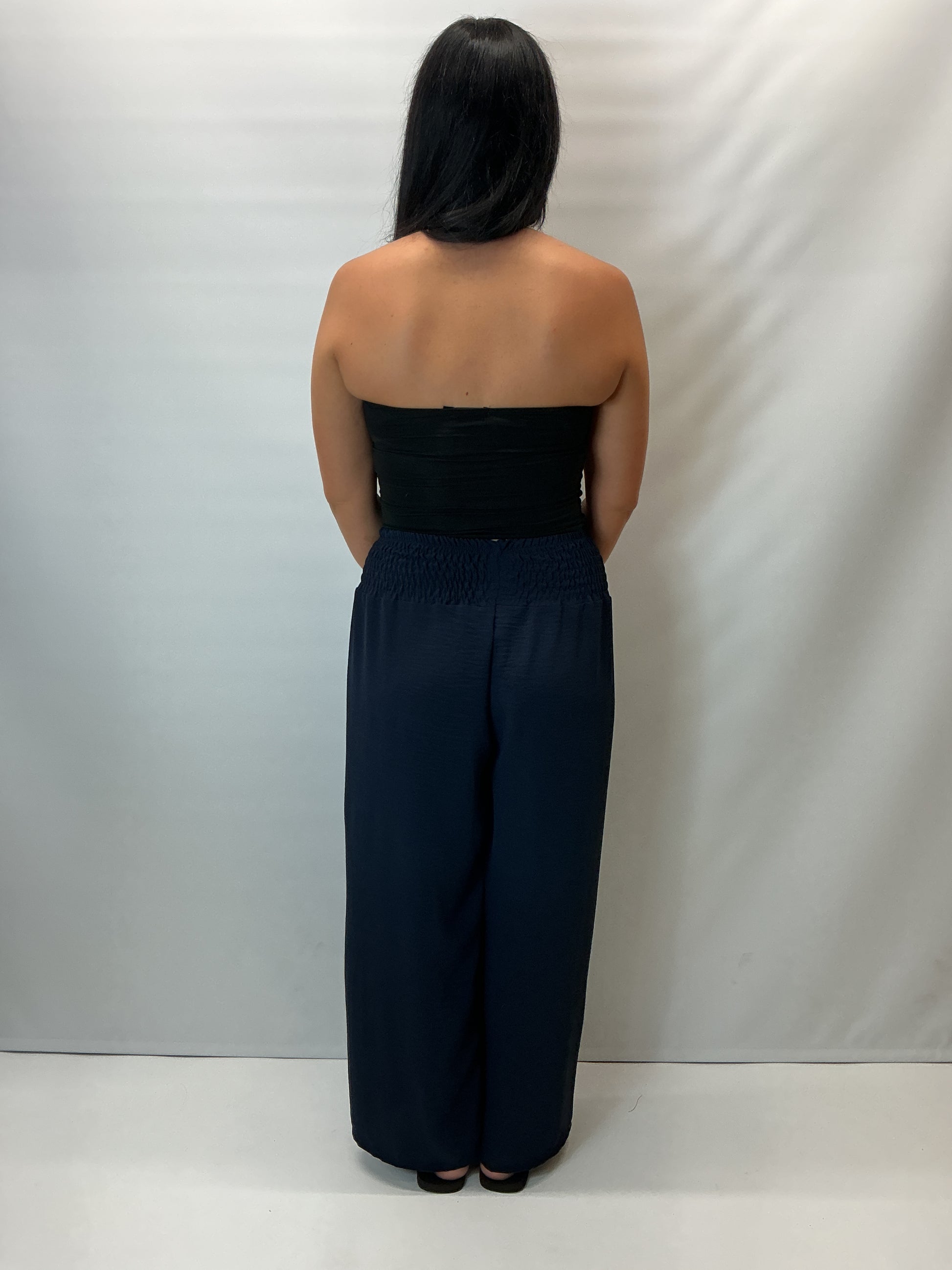 Navy smocked waist wide leg trousers with a relaxed fit, shown on a model wearing a fitted black halter top.