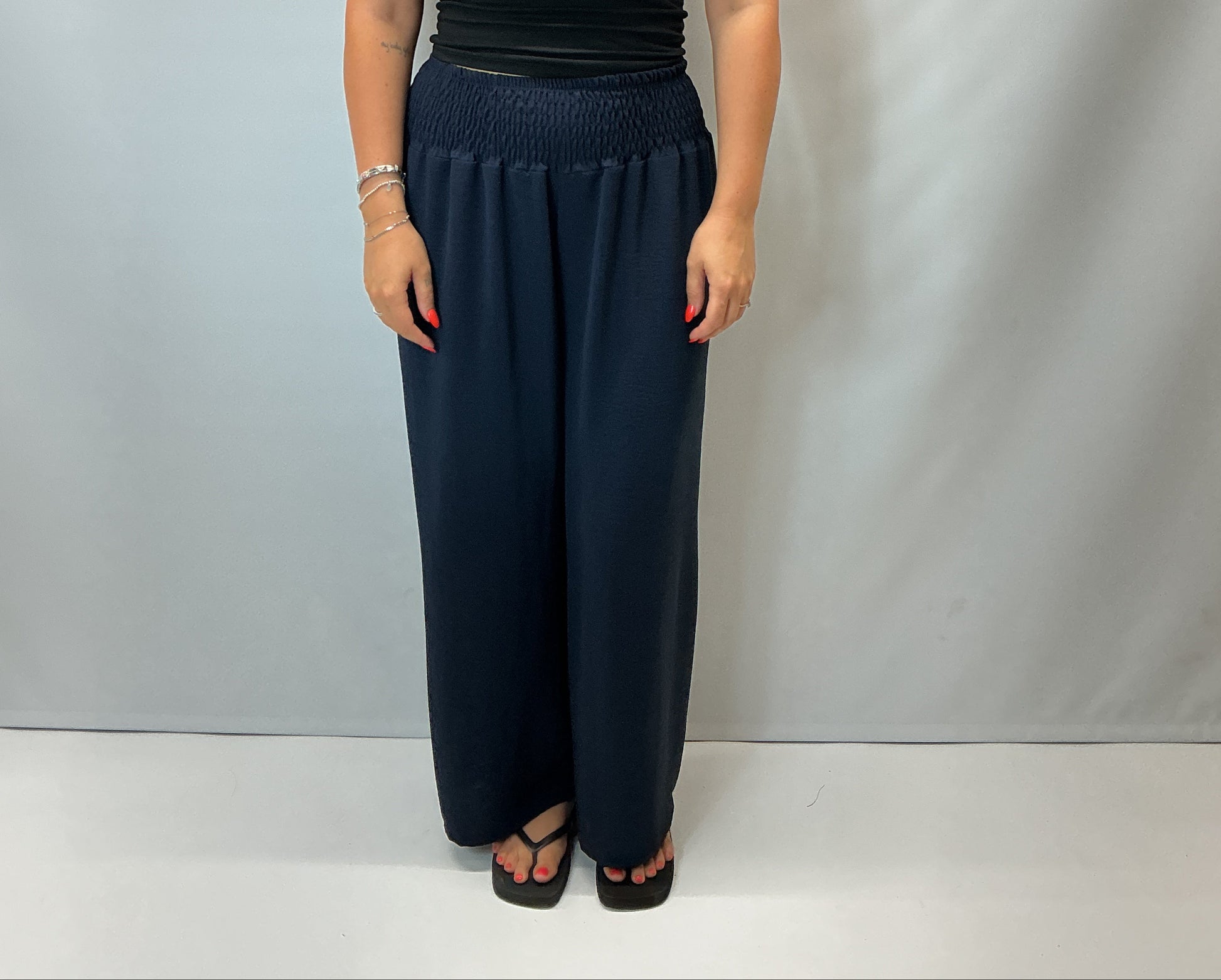 Navy smocked waist wide leg trousers with a relaxed fit, shown on a model wearing a fitted black halter top.