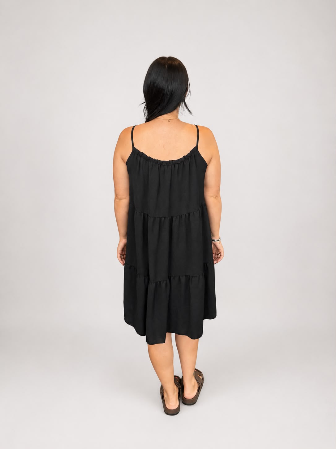 A versatile black tiered cami dress featuring spaghetti straps, a relaxed, flowy fit, and a flattering knee-length design. Lightweight and easy to wear, it's ideal for casual everyday styling, holidays, weekends, and warm-weather occasions.