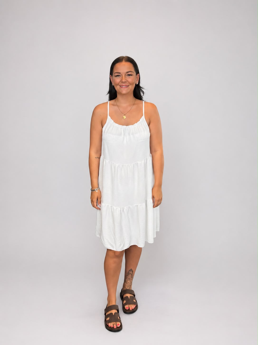 A versatile White tiered cami dress featuring spaghetti straps, a relaxed, flowy fit, and a flattering knee-length design. Lightweight and easy to wear, it's ideal for casual everyday styling, holidays, weekends, and warm-weather occasions.