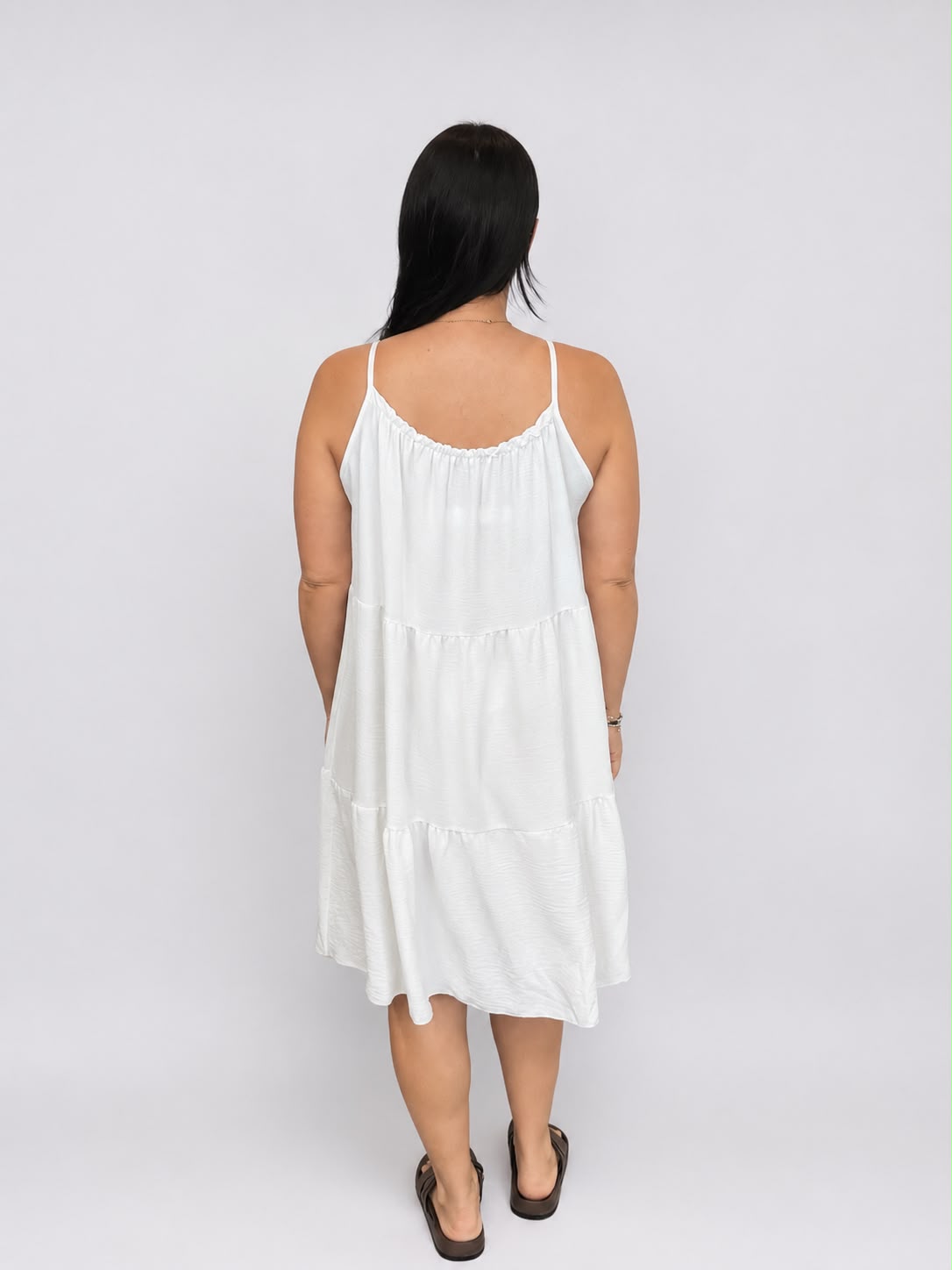 A versatile White tiered cami dress featuring spaghetti straps, a relaxed, flowy fit, and a flattering knee-length design. Lightweight and easy to wear, it's ideal for casual everyday styling, holidays, weekends, and warm-weather occasions.