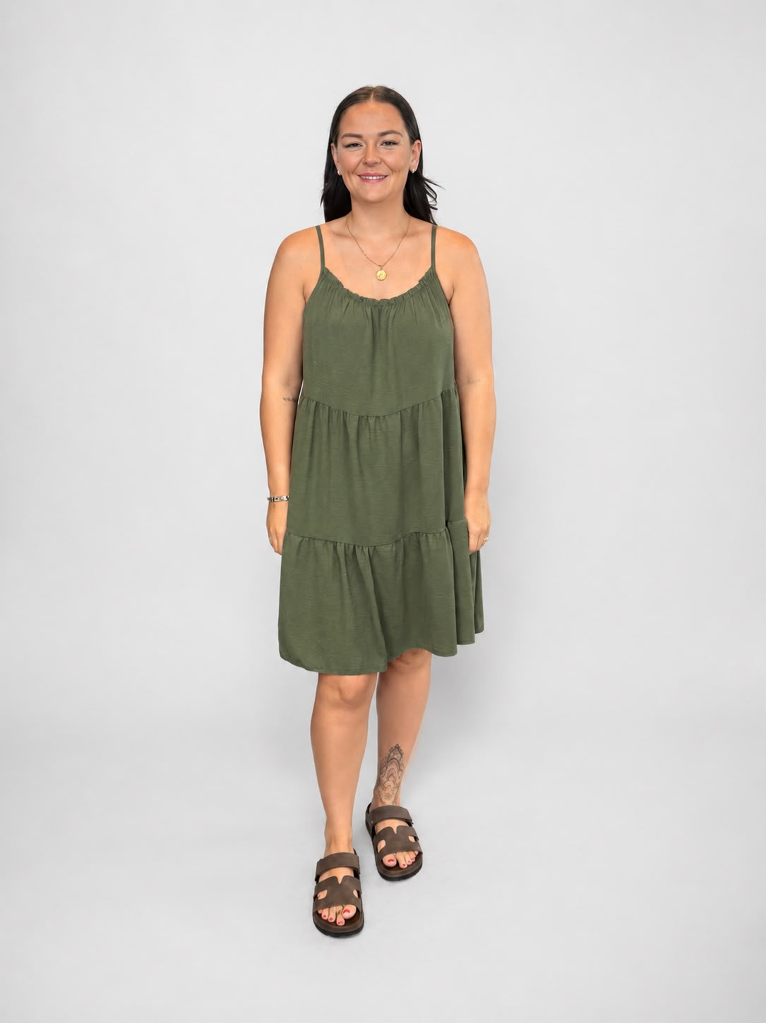A versatile khaki tiered cami dress featuring spaghetti straps, a relaxed, flowy fit, and a flattering knee-length design. Lightweight and easy to wear, it's ideal for casual everyday styling, holidays, weekends, and warm-weather occasions.