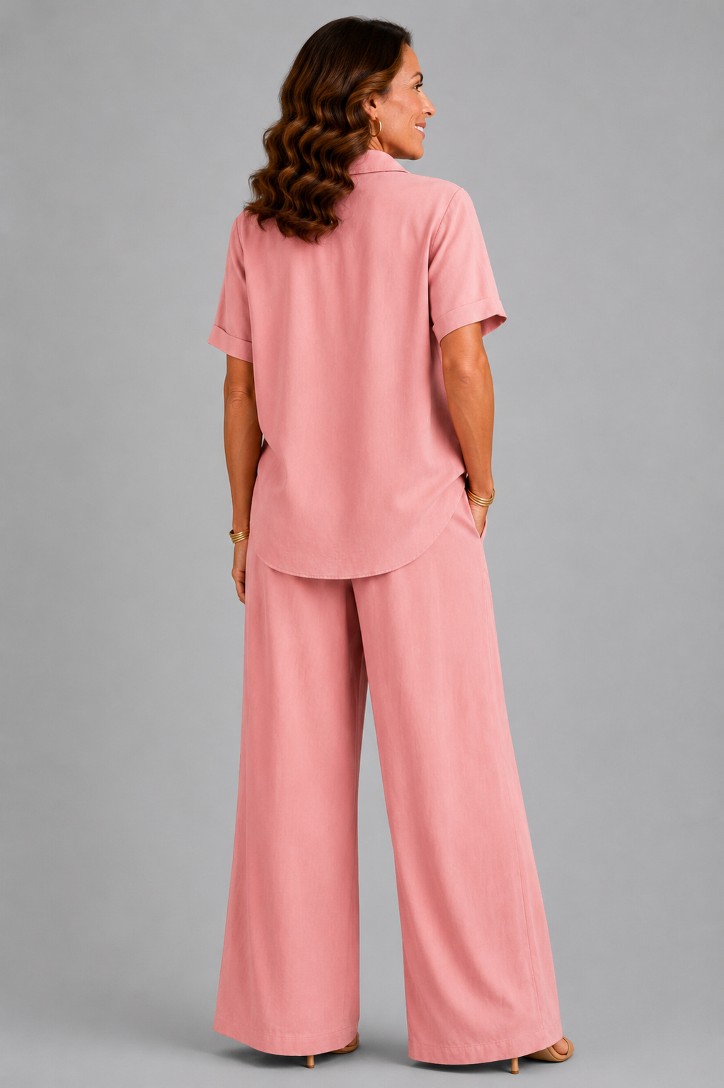 A smiling woman models a relaxed-fit Italian two-piece co-ord set on a light grey studio background. The outfit features a collared short-sleeve top with a detachable patterned scarf and matching wide-leg trousers. Shown in multiple colourways including black, cornflower blue, powder blue, sage green, blush pink and lemon yellow, the set offers an elegant, comfortable silhouette ideal for everyday wear and special occasions.