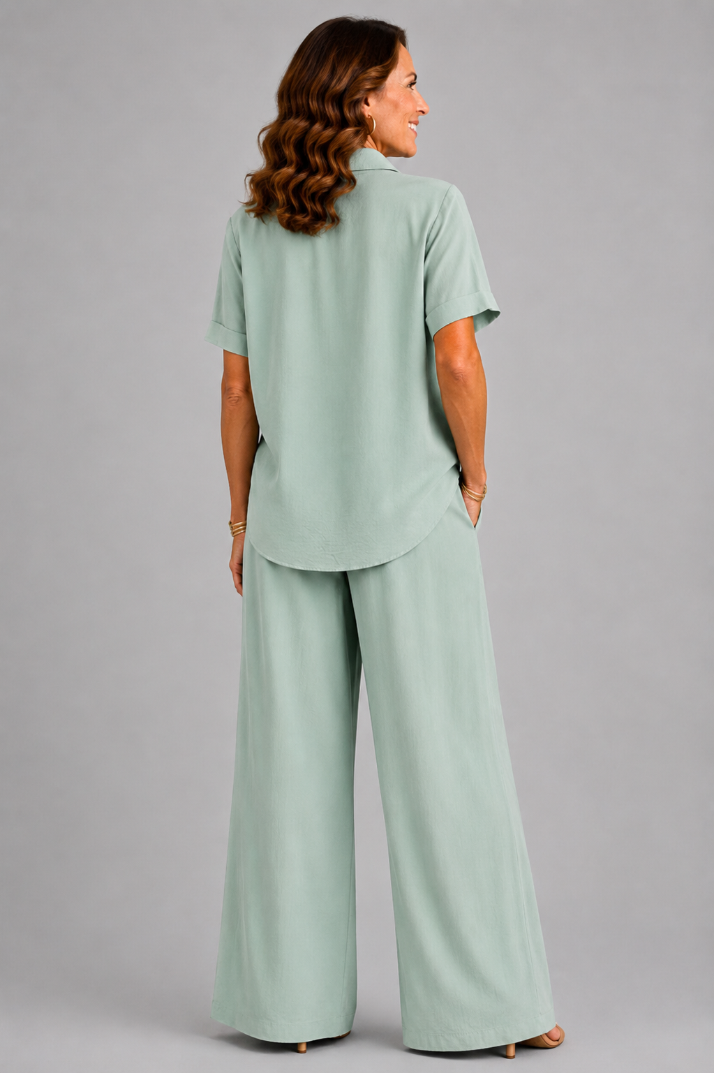 A smiling woman models a relaxed-fit Italian two-piece co-ord set on a light grey studio background. The outfit features a collared short-sleeve top with a detachable patterned scarf and matching wide-leg trousers. Shown in multiple colourways including black, cornflower blue, powder blue, sage green, blush pink and lemon yellow, the set offers an elegant, comfortable silhouette ideal for everyday wear and special occasions.