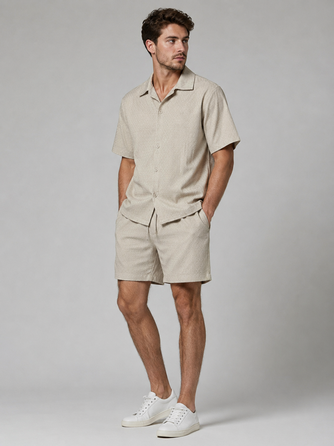 Men’s beige textured shirt and shorts co-ord set with short sleeve button-up shirt, drawstring shorts, and white trainers.