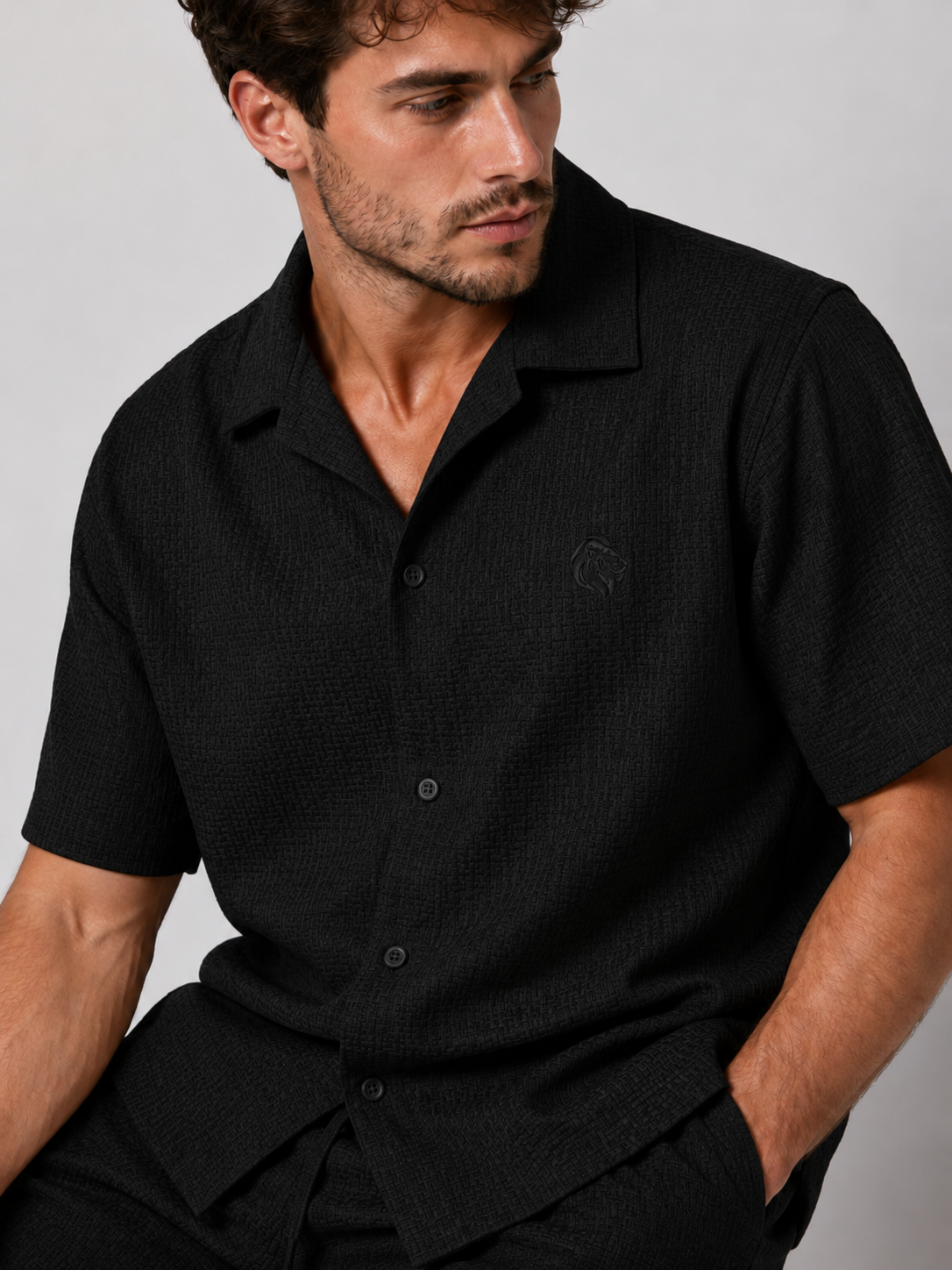 Men’s black textured shirt and shorts co-ord set with short sleeve button-up shirt, drawstring shorts, and white trainers.