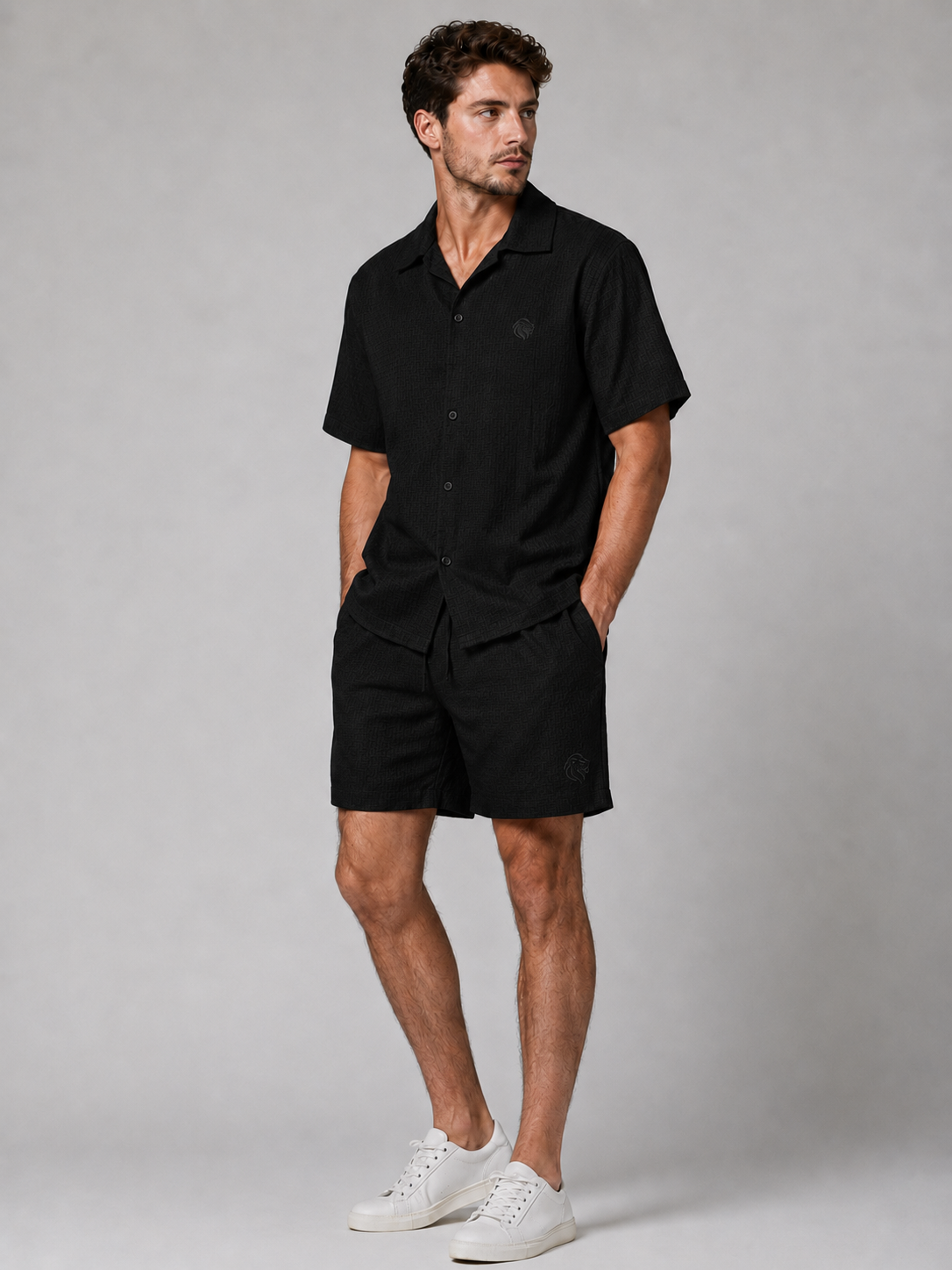 Men’s black textured shirt and shorts co-ord set with short sleeve button-up shirt, drawstring shorts, and white trainers.