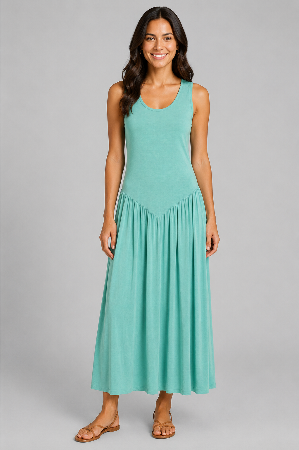 Women's sleeveless maxi dress featuring a scoop neckline, fitted bodice, and flowing gathered skirt. Shown in a soft brown jersey fabric with a relaxed silhouette and maxi length, styled on a model against a light grey studio background.