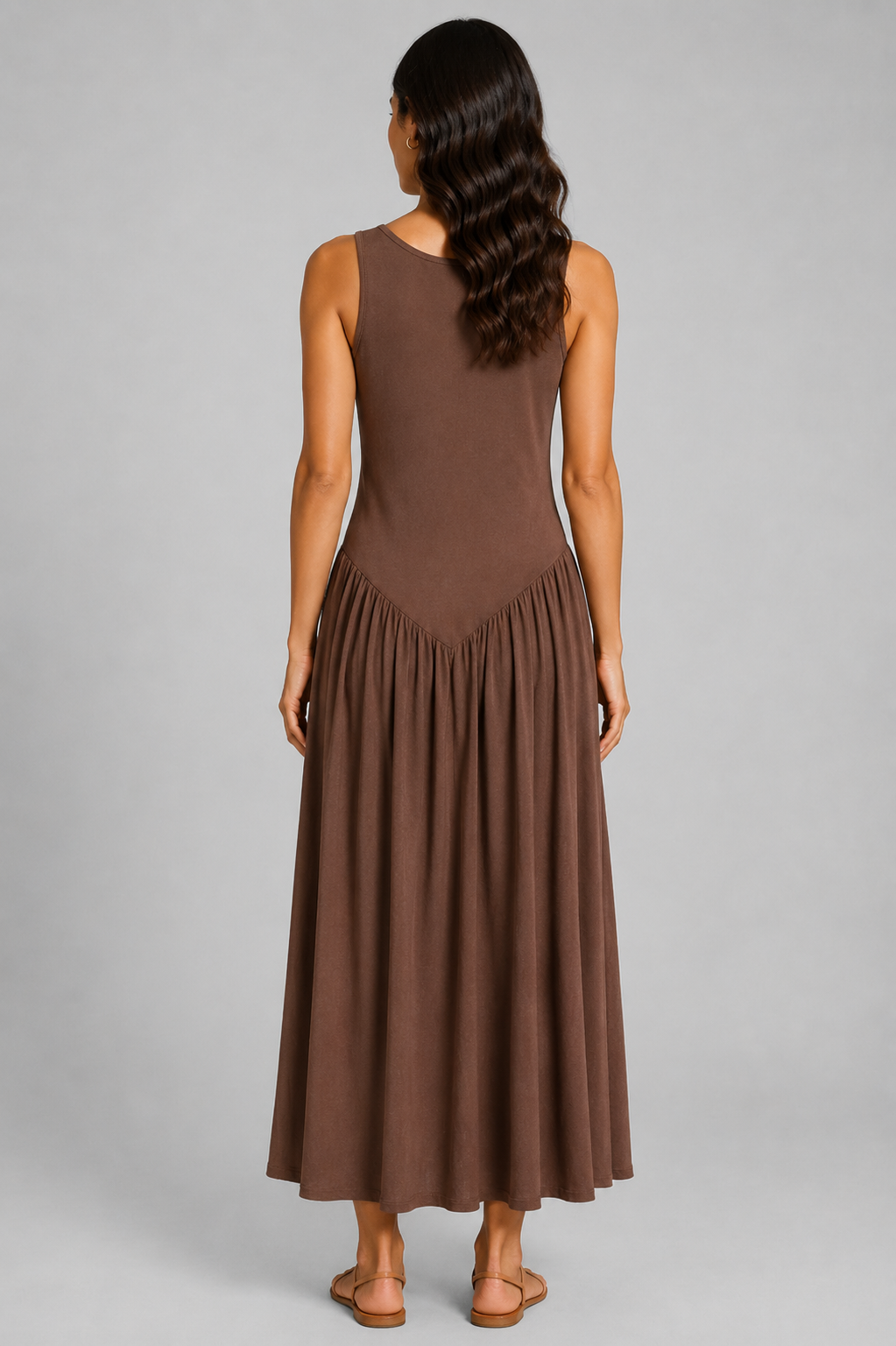Women's sleeveless maxi dress featuring a scoop neckline, fitted bodice, and flowing gathered skirt. Shown in a soft brown jersey fabric with a relaxed silhouette and maxi length, styled on a model against a light grey studio background.