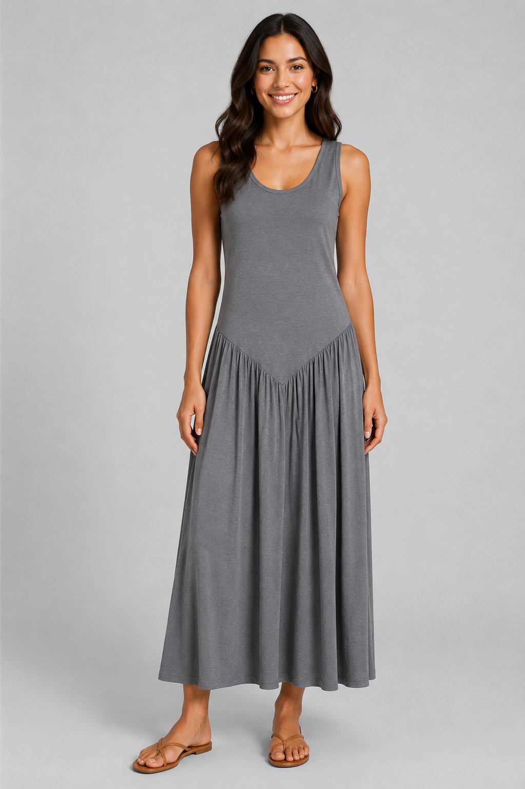 Women's sleeveless maxi dress featuring a scoop neckline, fitted bodice, and flowing gathered skirt. Shown in a soft brown jersey fabric with a relaxed silhouette and maxi length, styled on a model against a light grey studio background.