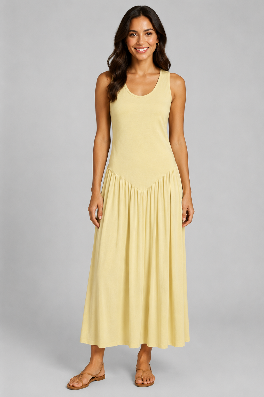 Women's sleeveless maxi dress featuring a scoop neckline, fitted bodice, and flowing gathered skirt. Shown in a soft brown jersey fabric with a relaxed silhouette and maxi length, styled on a model against a light grey studio background.