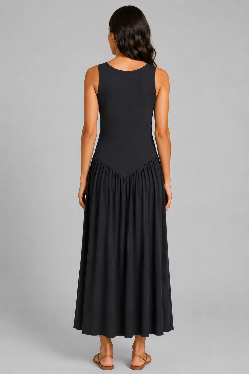 Women's sleeveless maxi dress featuring a scoop neckline, fitted bodice, and flowing gathered skirt. Shown in a soft brown jersey fabric with a relaxed silhouette and maxi length, styled on a model against a light grey studio background.