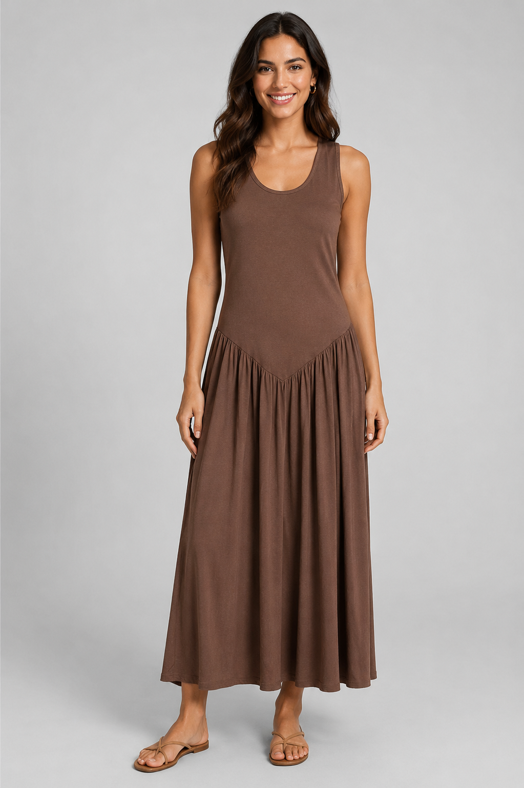 Women's sleeveless maxi dress featuring a scoop neckline, fitted bodice, and flowing gathered skirt. Shown in a soft brown jersey fabric with a relaxed silhouette and maxi length, styled on a model against a light grey studio background.